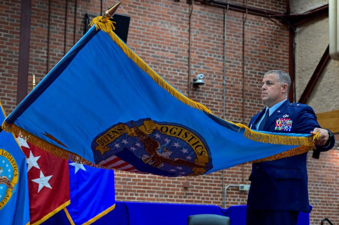 A one-star Air Force General standing on stage during a ceremony holding a command flag