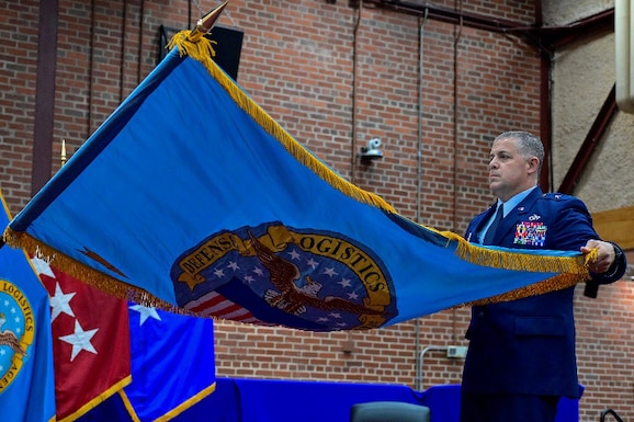 A one-star Air Force General standing on stage during a ceremony holding a command flag