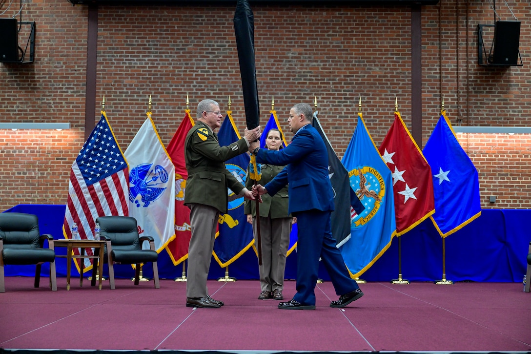 Three military service members standing on stage during a ceremony rolling a command flag