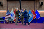 Three military service members standing on stage during a ceremony rolling a command flag