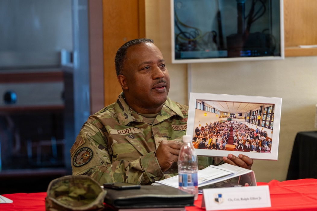 U.S. Air Force Col. Ralph Elliott, Europe-Air Forces Africa command chaplain, holds a framed photo of a congregation while speaking with members of the 52nd Fighter Wing Chapel during a visit to Spangdahlem Air Base, Germany, June 24, 2026. Elliot highlighted the importance of chapel engagement in fostering community, resilience and spiritual readiness among airman and their families.