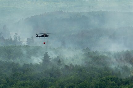 A U.S. Army National Guard UH-60 Black Hawk helicopter assigned to the 34th Combat Aviation Brigade transports water in a water bucket over wildfires in Northern Minnesota, July 15, 2026.