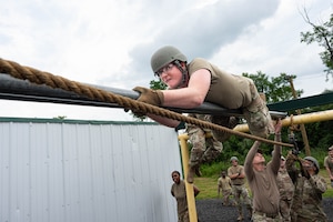 U.S. Air Force Airman 1st Class Brock Ramey, 436th Civil Engineering Squadron water and fuel systems maintenance apprentice, climbs across a pole during a leadership course obstacle at Fort Indiantown Gap, Pennsylvania, July 7, 2026.