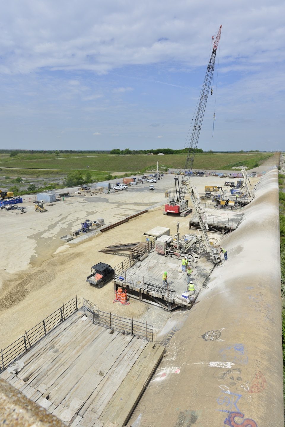 Construction crews drilling one of more than 70 high-capacity post-tensioned anchors through the spillway weir and into the underlying bedrock. These anchors increase the spillway's resistance to uplift forces and improve overall structural stability. This is one of many improvements being made as part of the Lewisville Spillway Modification Program. In addition, engineers installed an upstream geomembrane blanket designed to limit seepage beneath the spillway, reducing water pressures that can develop beneath the concrete during flood operations. Additional improvements include reinforcing portions of the spillway apron with 936 rock dowels and restoring disturbed areas once construction is complete.