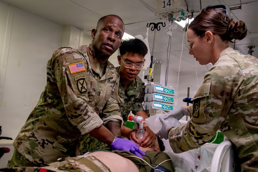 Three people dressed in camouflage military uniforms tend to a simulated casualty during a mass casualty exercise.