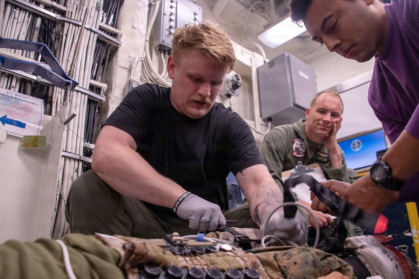 Two men tend to a simulated casualty while another man observes during a mass casualty exercise.