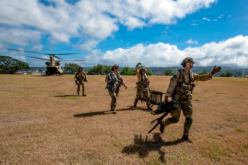 Four people wearing camouflage military uniforms run from a helicopter during a mass casualty exercise.
