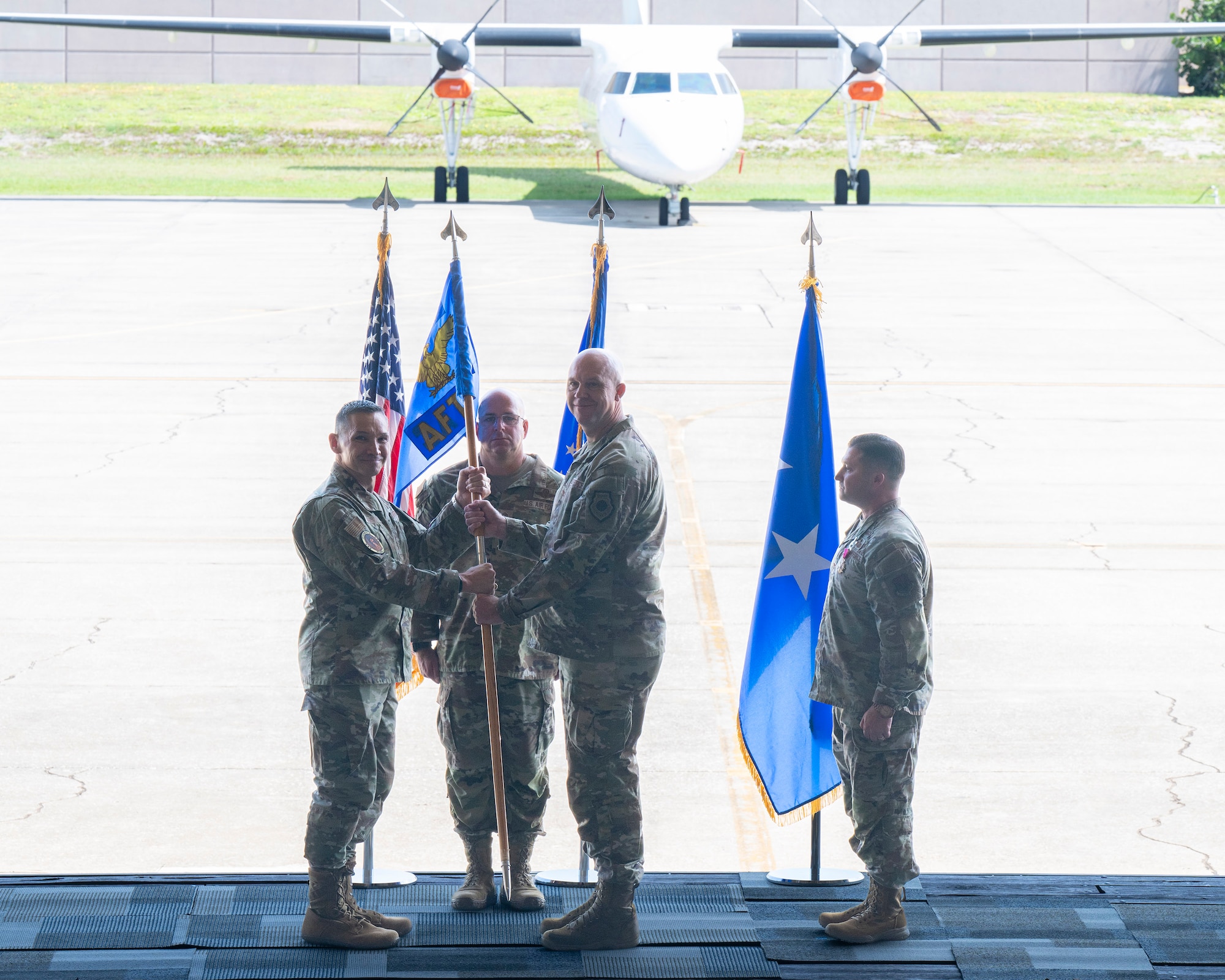 Lt. Gen. Thomas K. Hensley, (left) commander of 16th Air Force (Air Forces Cyber) passes the Air Force Technical Applications Center’s guidon to Col. Mark Brow who took command of the center at a Change of Command ceremony July 24, 2026 at Patrick Space Force Base, Fla.  Also pictured are Col. Creighton Mullins (far right), AFTAC’s outgoing commander, and Chief Master Sgt. Brandon Bitler, guidon bearer and AFTAC’s Command Chief. (U.S. Air Force photo by Matthew S. Jurgens)