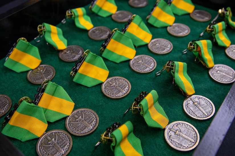 Circular metallic medals attached to green- and yellow-striped ribbons sit in rows against dark green fabric.