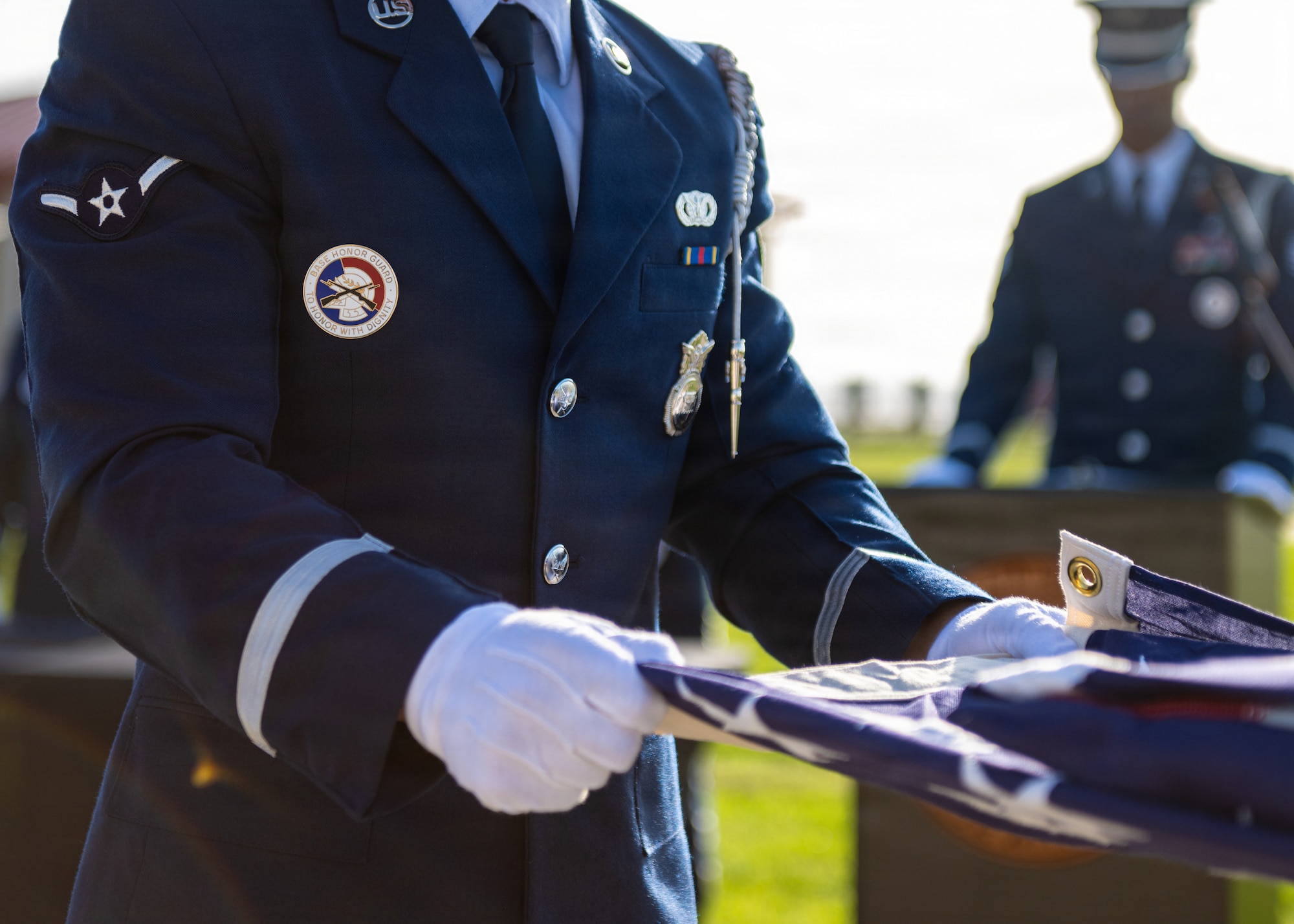 A U.S. Air Force ceremonial guardsman assigned to the 6th Force Support Squadron assists in folding a ceremonial U.S. flag during a base honor guard induction ceremony at MacDill Air Force Base, Florida, July 22, 2026. Ceremonial guardsmen do not wear a nametape on their uniform to honor the fallen service member without personal recognition. (U.S. Air Force photo by Senior Airman Derrick Bole)