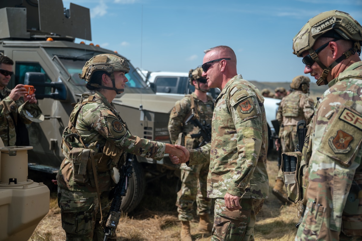 Two military members in camouflage uniform shake hands.