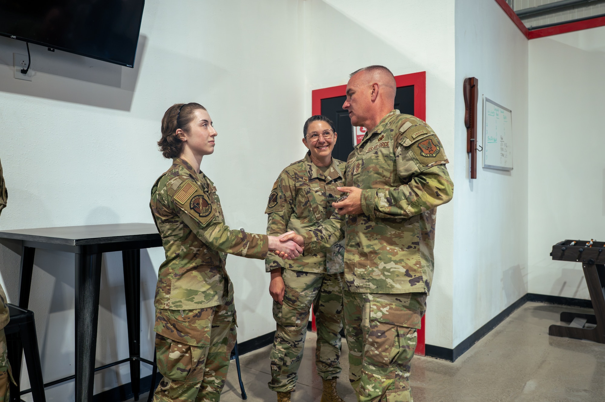 Two military members wearing camouflage uniforms shake hands.