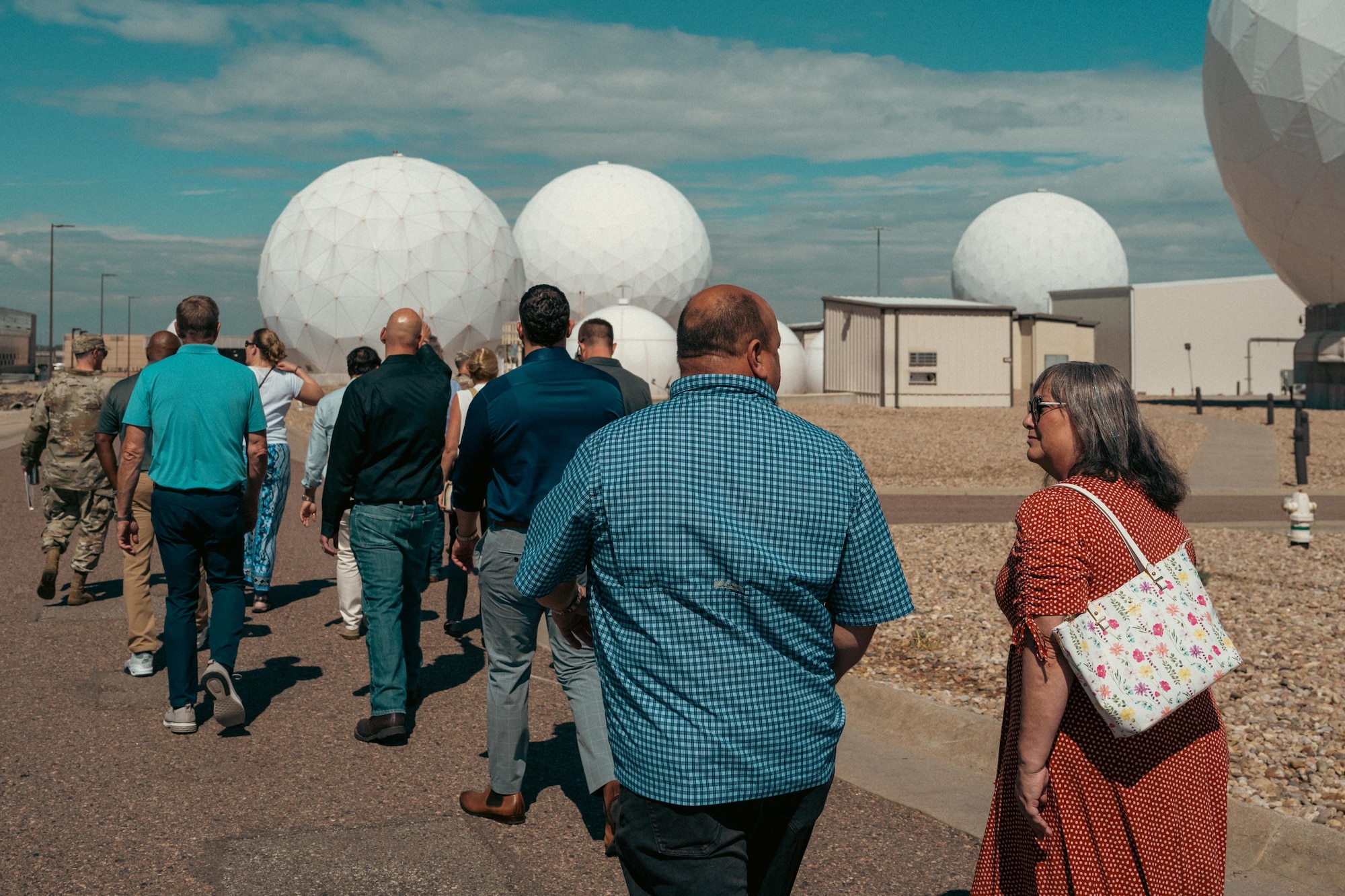 a group of people walk towards a cluster of 3 radomes