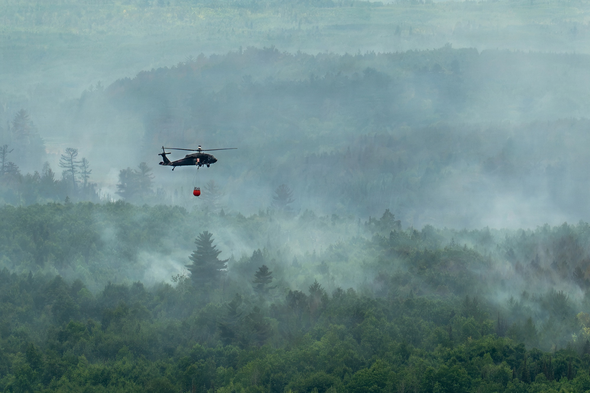 A U.S. Army National Guard UH-60 Black Hawk helicopter assigned to the 34th Combat Aviation Brigade transports water in a water bucket over wildfires in Northern Minnesota, July 15, 2026.