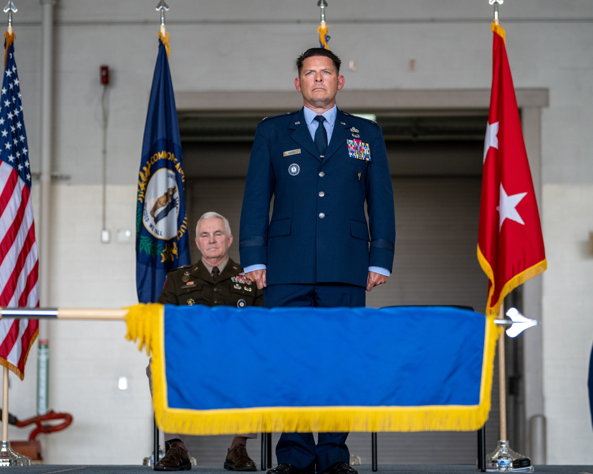 Newly promoted Brig. Gen. Ash Groves looks on as the 123rd Airlift Wing Honor Guard unfurls a brigadier general’s flag during his promotion ceremony at the Kentucky Air National Guard Base in Louisville, Ky., June 7, 2026. Groves, who previously served as director of the Air staff at Joint Force Headquarters-Kentucky, is now chief of the Air staff at JFHQ-KY. (U.S. Air National Guard photo by Senior Airman Annaliese Billings)