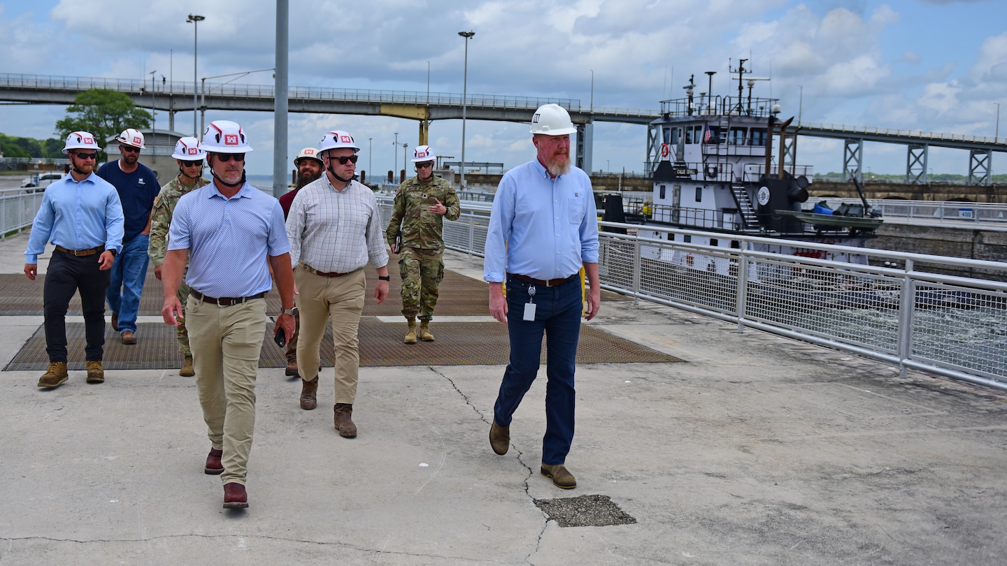 Adam Telle (Third from Right), assistant secretary of the Army for Civil Works, is joined by U.S. Army Corps of Engineers and Tennessee Valley Authority leaders, lock operators, maintainers, and engineers during a site visit July 20, 2026, at Wilson Lock on the Tennessee River in Florence, Alabama. The Motor Vessel Callie Devall is seen in the background locking through the navigation lock with barges. (USACE Photo by Lee Roberts)