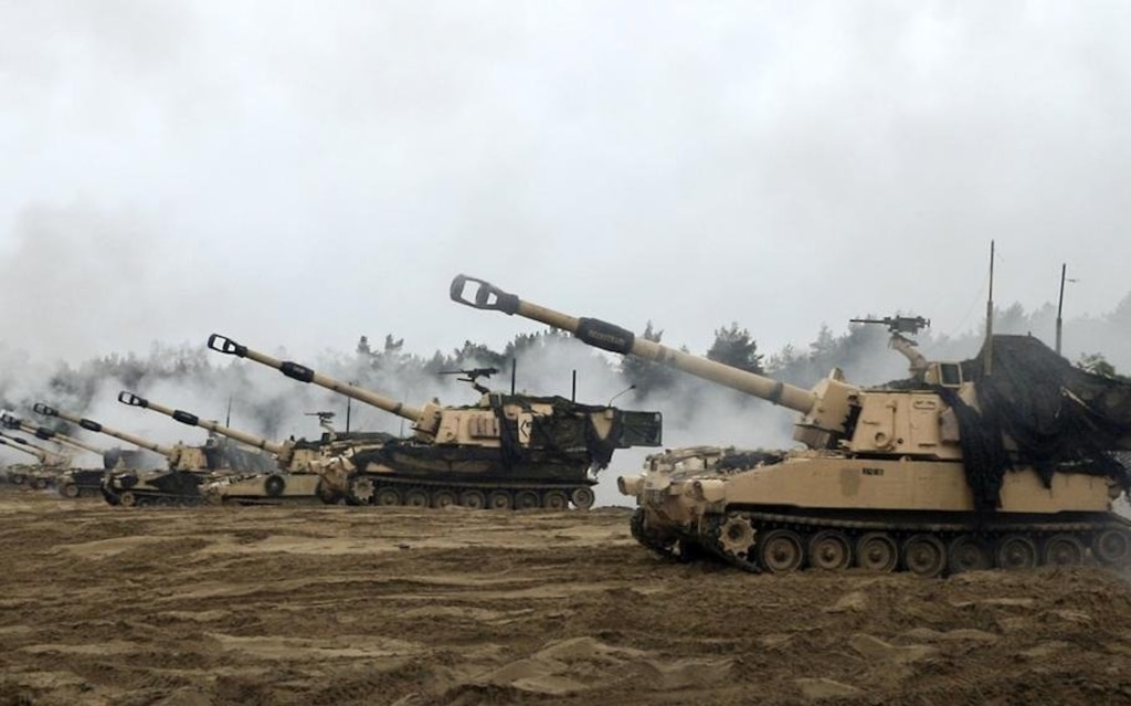 Multiple armored tanks aligned in a formation, conducting a live-fire exercise on an open training range.