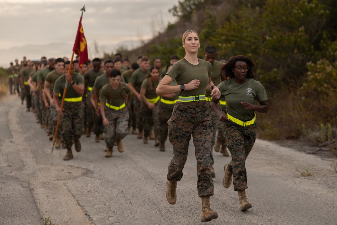 U.S. Marine Corps Maj. Valentine, center, commanding officer of Alpha Company, Headquarters and Support Battalion, Marine Corps Installations West, and 1st Sgt. Britinay N. Burke, company first sergeant with Alpha Co., lead Marines with Alpha Co. and with Corporals Course 4-26 on a trail run at Marine Corps Base Camp Pendleton, Calif.. During the run, Marines read citations for Medal of Honor recipients to remember and honor Marines and Sailors from the past. (U.S. Marine Corps photo by Sgt. Buck)