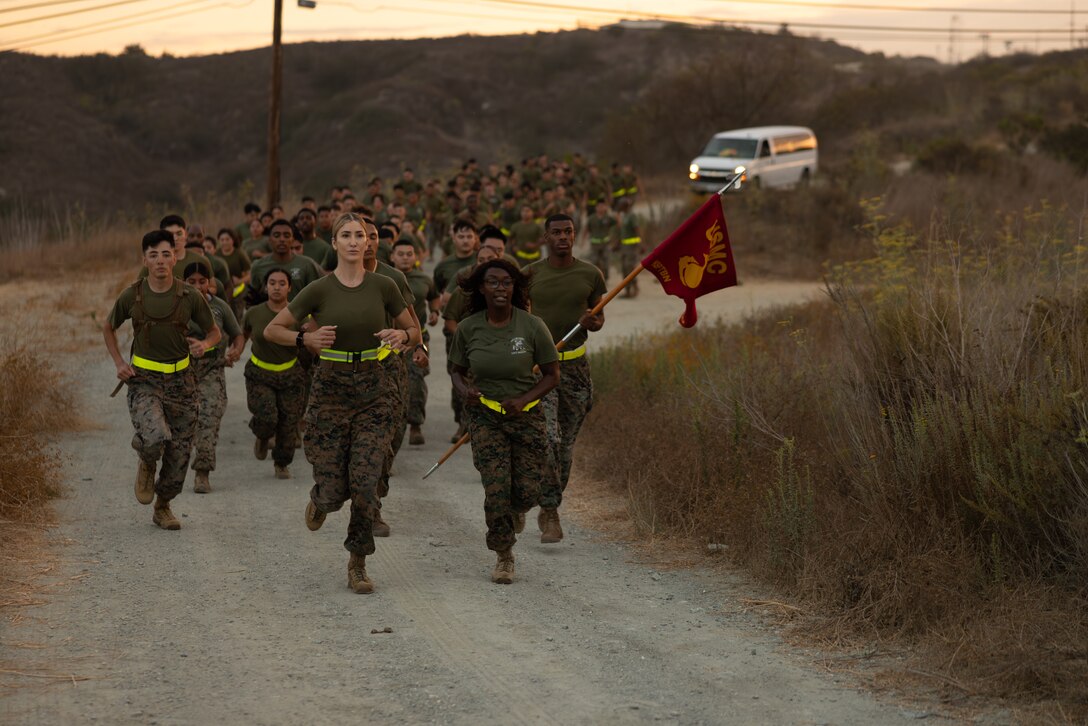 U.S. Marine Corps Maj.  Valentine, center, commanding officer of Alpha Company, Headquarters and Support Battalion, Marine Corps Installations West, and 1st Sgt. Britinay N. Burke, company first sergeant with Alpha Co., lead Marines with Alpha Co. and with Corporals Course 4-26 on a trail run at Marine Corps Base Camp Pendleton, Calif.,. During the run, Marines read citations for Medal of Honor recipients to remember and honor Marines and Sailors from the past. (U.S. Marine Corps photo by Sgt. Buck)