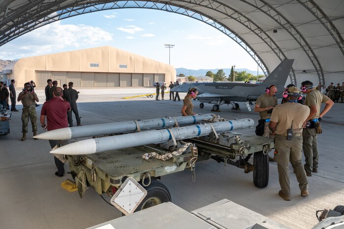 Airmen gather below a hangar with a YFQ-44A Fury aircraft and missiles in the vicinity.