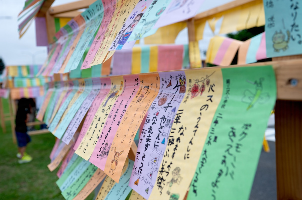 Colorful strips of paper adorned with written hopes and wishes hang off of a wooden frame