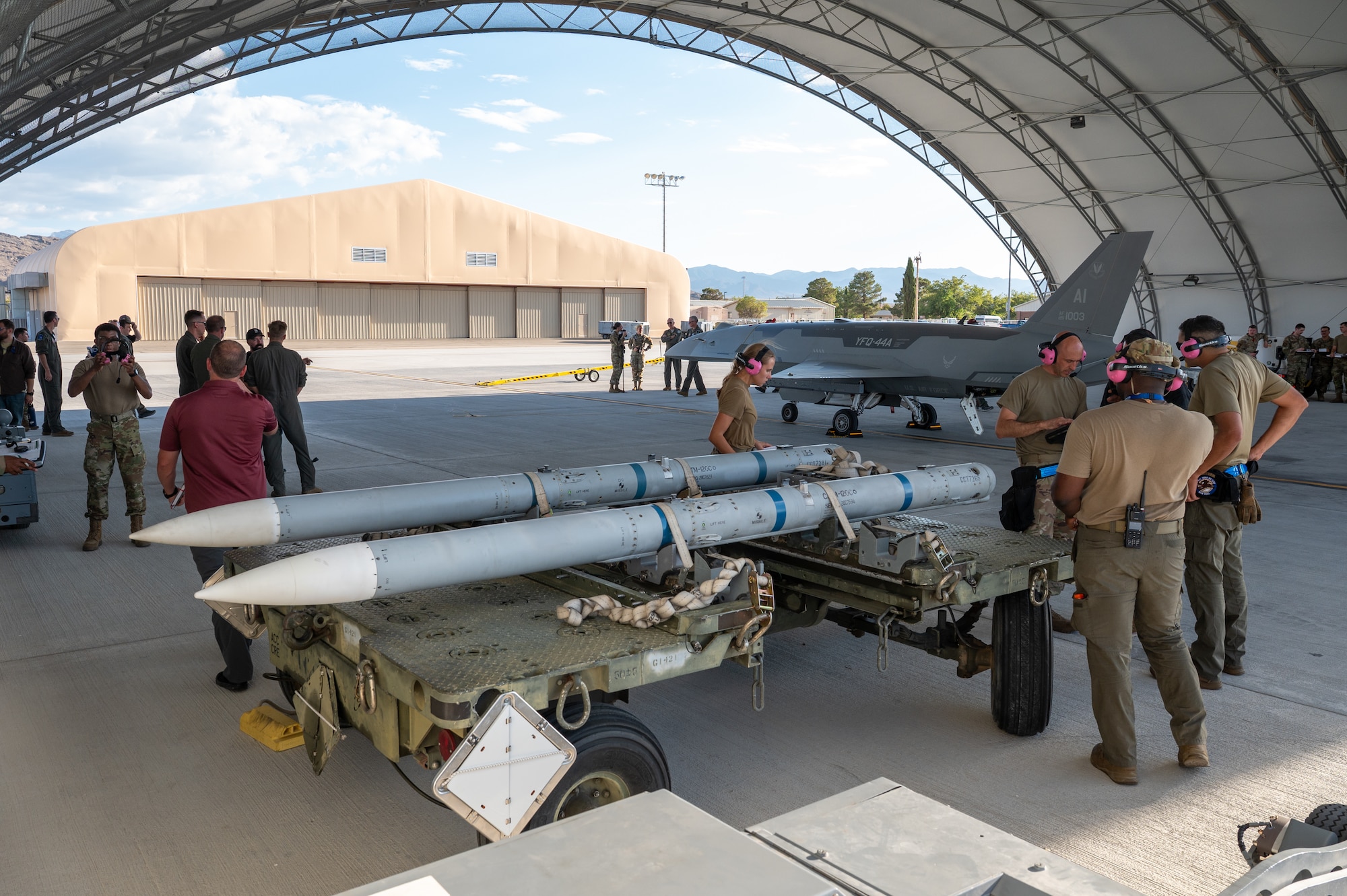 Airmen gather below a hangar with a YFQ-44A Fury aircraft and missiles in the vicinity.