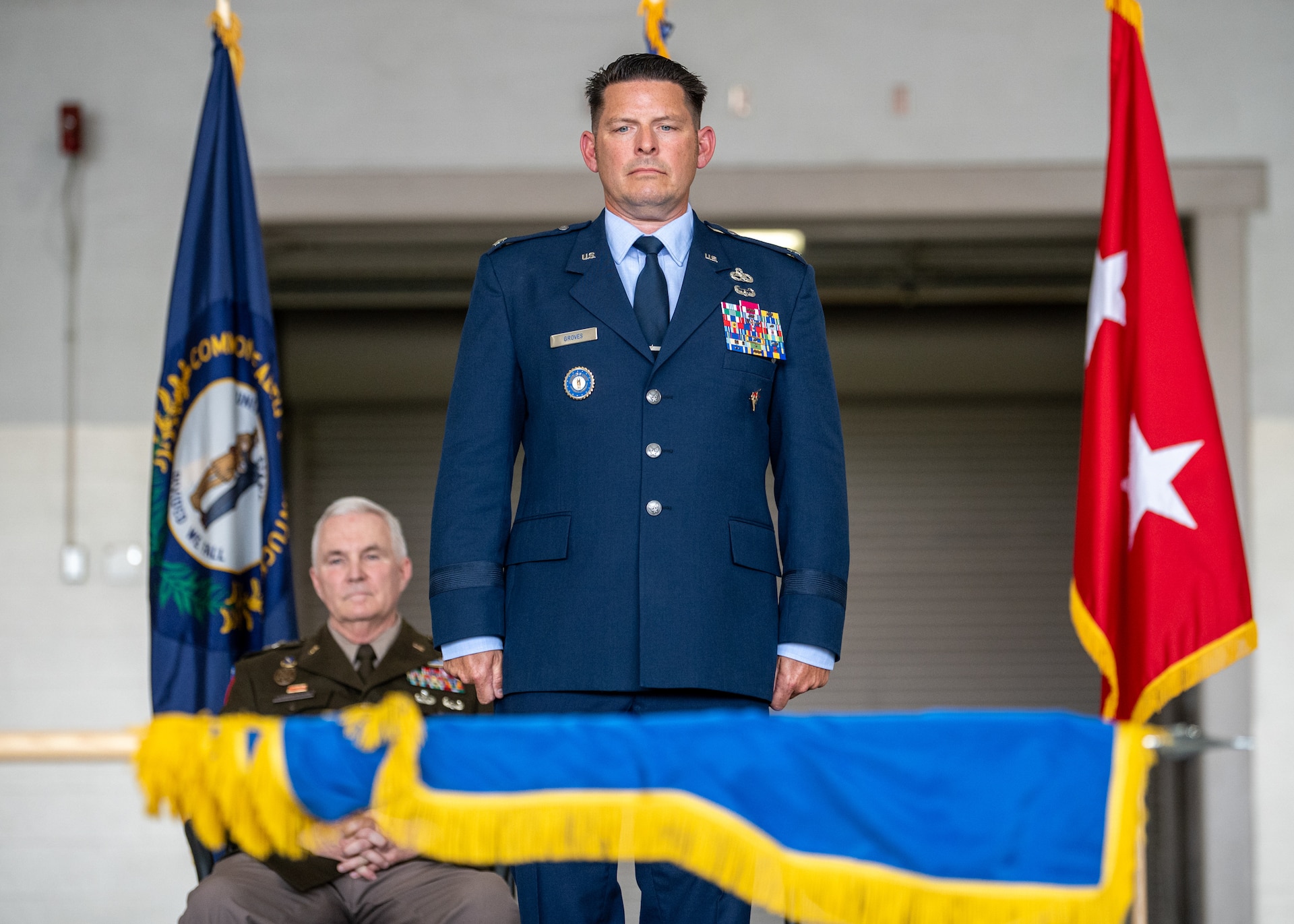 Newly promoted Brig. Gen. Ash Groves looks on as the 123rd Airlift Wing Honor Guard unfurls a brigadier general’s flag during his promotion ceremony at the Kentucky Air National Guard Base in Louisville, Ky., June 7, 2026. Groves, who previously served as director of the Air staff at Joint Force Headquarters-Kentucky, is now chief of the Air staff at JFHQ-KY. (U.S. Air National Guard photo by Senior Airman Annaliese Billings)