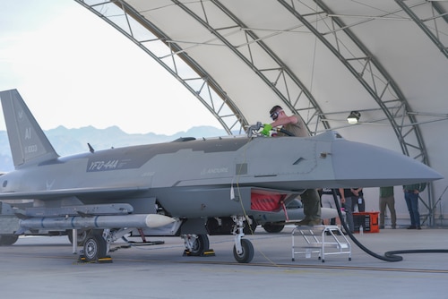 A U.S. Airman fuels a YFQ-44A Fury aircraft. The refueling opening is on top of the aircraft and the Airman is using a stool to reach the location.