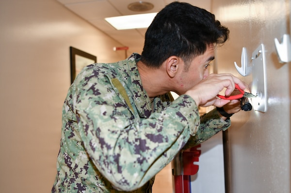 Navy Medicine Readiness and Training Command Pensacola Sailor, Hospital Corpsman 2nd Class, Biomedical Equipment Technician, Brentkyle Cabrero, assigned to Naval Hospital Pensacola, inspects an in-wall wiring connection, Naval Branch Health Clinic Naval Air Station Pensacola, Pensacola, Florida, June 24, 2026. From the fleet to clinics Biomedical Equipment Technicians are specialized Hospital Corpsmen that install, maintain and repair medical equipment ensuring equipment is safe to use for patient care. (U.S. Navy photo by Mass Communication Specialist Seaman Jon Jezreel Andres)