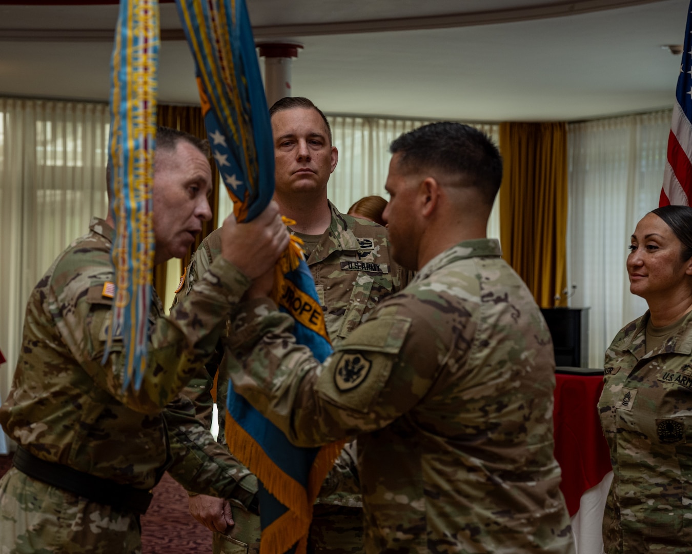 U.S. Army Brig. Gen. Sean P. Kelly, DLA Troop Support commander (left) passes the unit colors to the incoming commander, Army Lt. Col. Alan Strange symbolizing that he has taken command of DLA Troop Support Europe & Africa, June 26, 2026, at The Armstrong Club, Kaiserslautern, Germany. Army Lt. Col. Eduardo Rivera relinquished command of the unit, which provides food, clothing, construction materials, medical supplies and more to warfighters throughout Europe, Africa and the Middle East. Department of War photograph by Anthony Sualog.