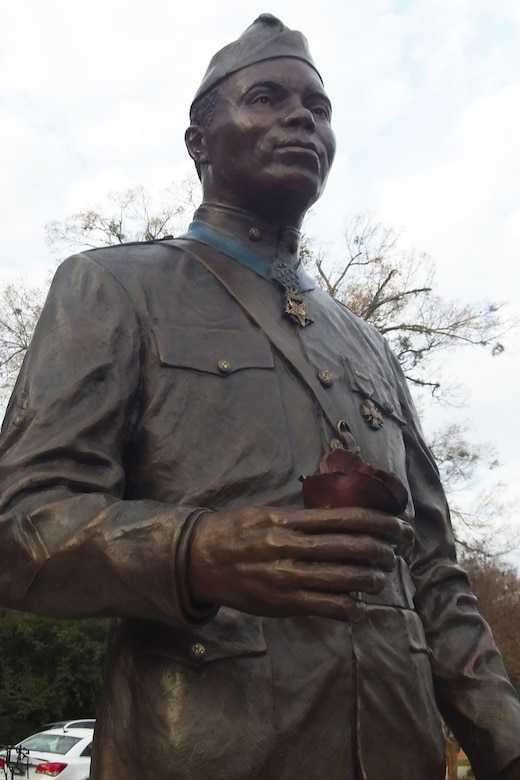 A bronze statue of a man in a World War I-era uniform and wearing a Medal of Honor stands outside.