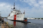 A tugboat maneuvers a Coast Guard cutter near a pier.