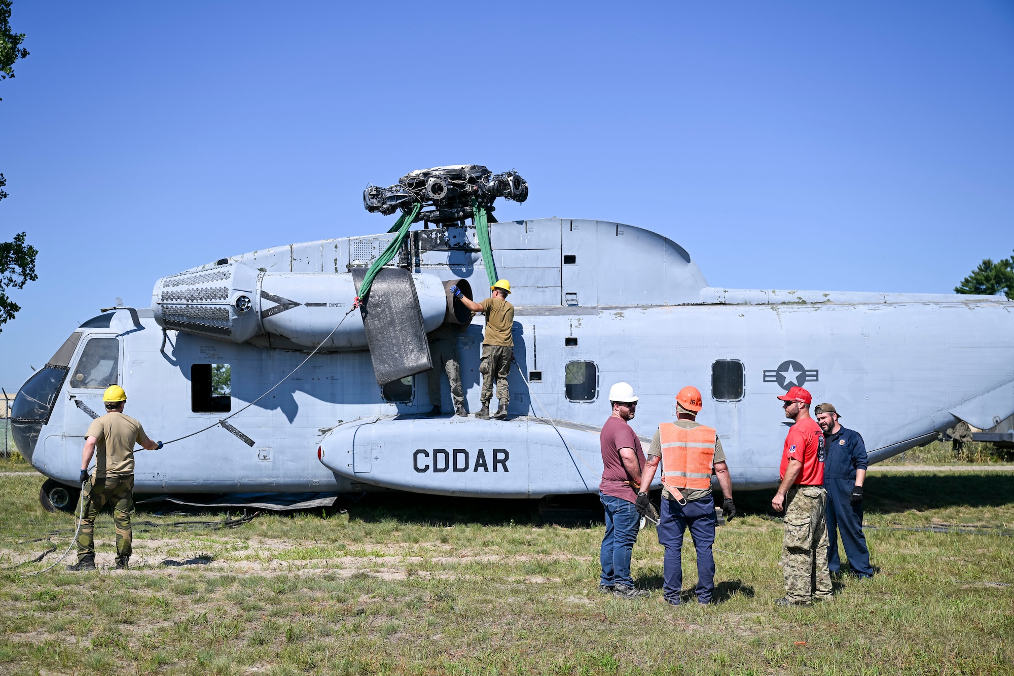 Aircraft recovery personnel from the U.S. Air Force, U.S. Marine Corps and U.S. Navy, alongside industry and allied partners, prepare a CH-53 helicopter to hoist an F-15 Eagle training aircraft during the F-35 Joint Program Office Advanced Crash Damaged or Disabled Aircraft Recovery (CDDAR) course at Volk Field Combat Readiness Training Center, Wisconsin, July 13, 2026. The advanced CDDAR course challenged participants to solve complex recovery scenarios while improving joint integration, critical thinking and multinational interoperability. (U.S. Air National Guard photo by Master Sgt. Regina Young)
