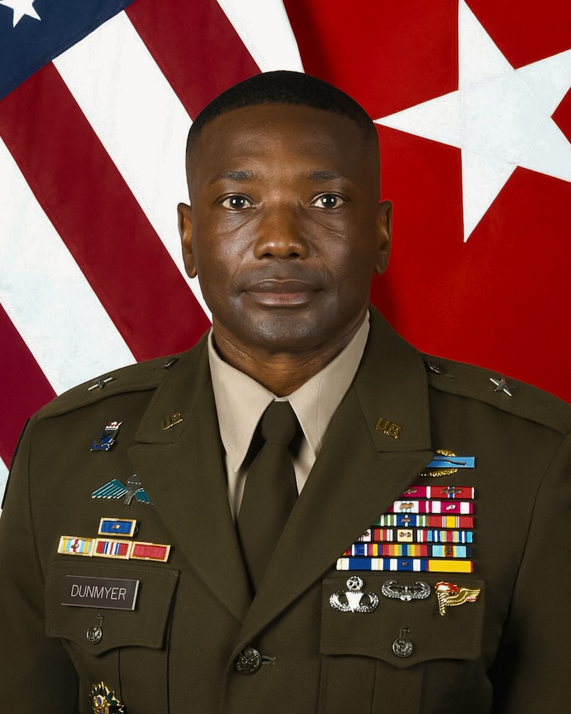 Headshot of BG Dunmyer, USAWC Commandant, smiling against a one star flag and American Flag.