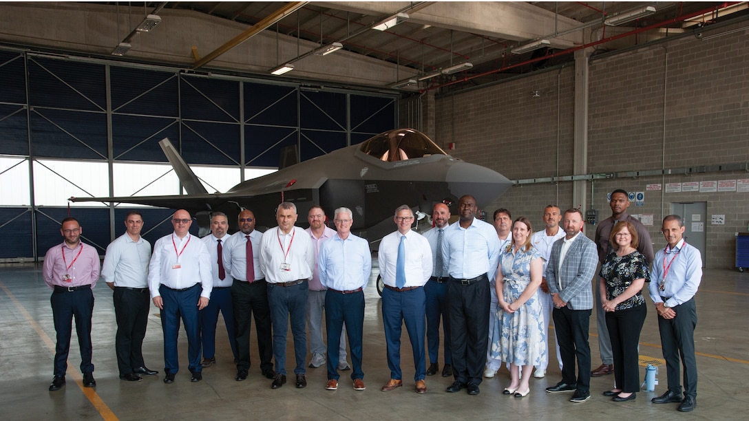 A group photo of international partners with an F-35 in the background.