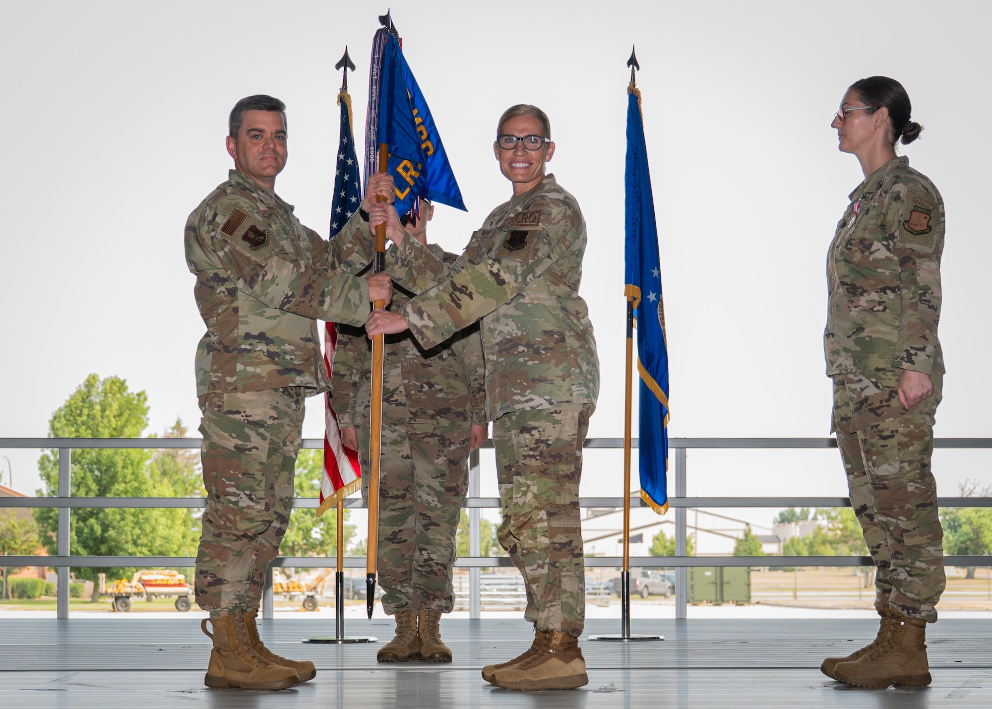 A photo of three people standing on a stage passing a guidon.