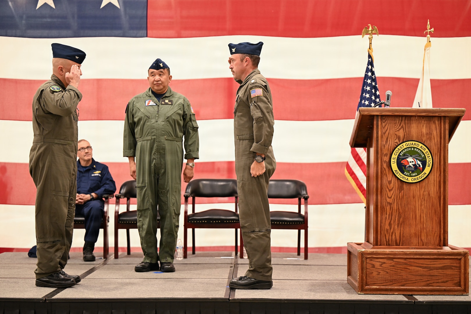 Capt. Neal Corbin (left) and Cmdr. Michael Flint (right) salute each other during Coast Guard Air Station Astoria’s change-of-command ceremony in Warrenton, Ore., July 16, 2026. Rear Adm. Arex B. Avanni (center) presided over the ceremony in which Flint relieved Corbin as Air Station Astoria’s commanding officer. (U.S. Coast Guard photo by Petty Officer 1st Class Lara Davis)