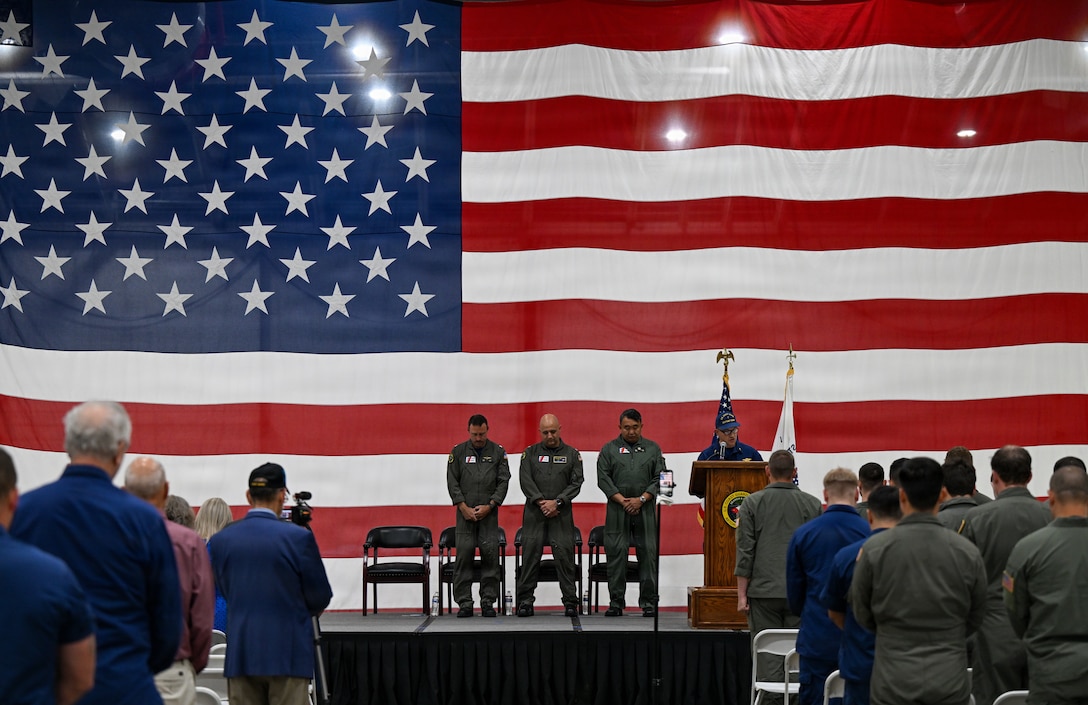 From left to right, Cmdr. Michael Flint, Capt. Neal Corbin, Rear Adm. Arex Avanni, and Chaplain Phillip Webster stand as Webster gives an invocation during Coast Guard Air Station Astoria’s change-of-command ceremony in Warrenton, Ore., July 16, 2026. During the ceremony, Flint relieved Corbin as commanding officer of Coast Guard Air Station Astoria. (U.S. Coast Guard Photo by Petty Officer 3rd Class William Kirk)