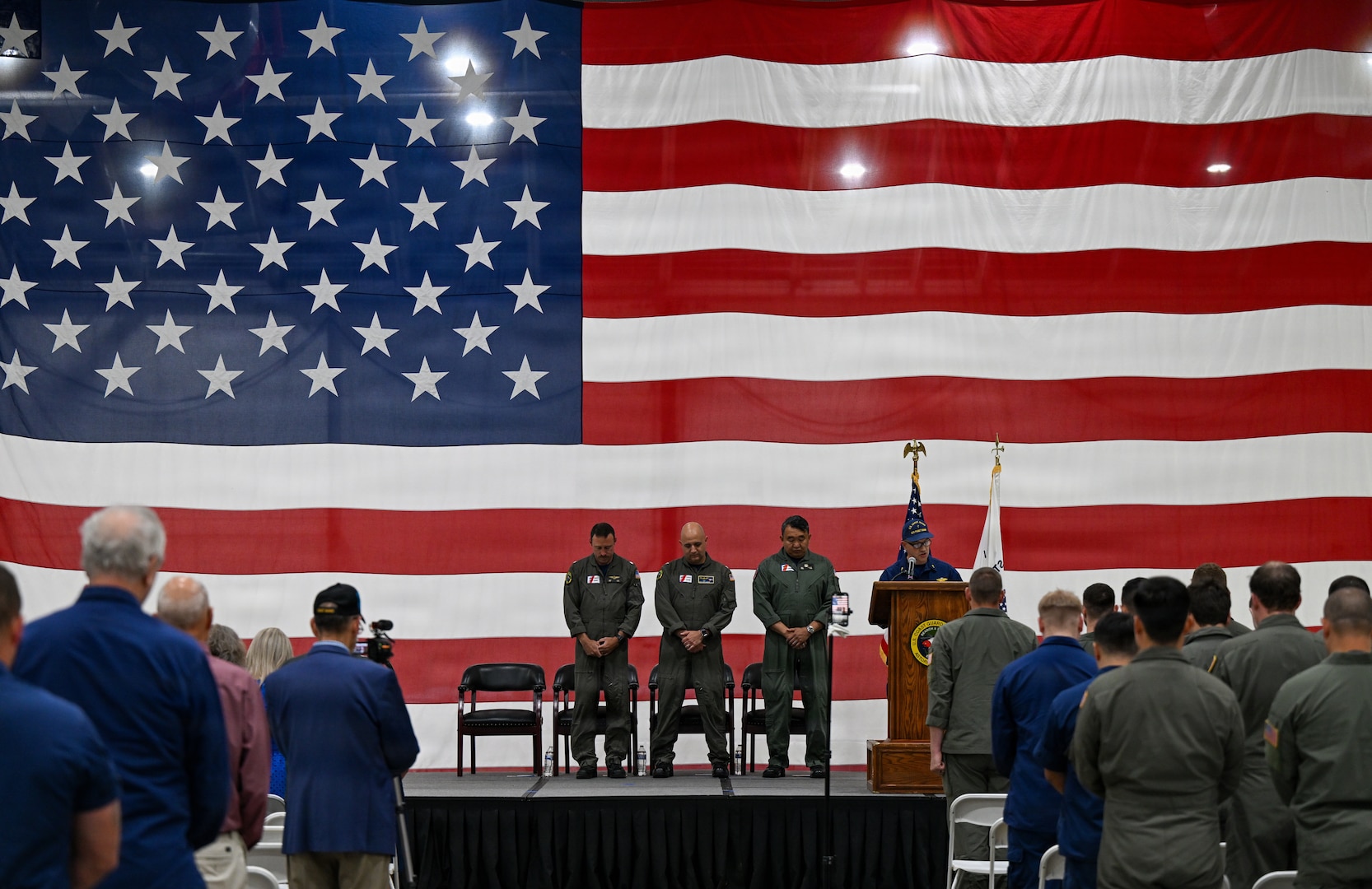 From left to right, Cmdr. Michael Flint, Capt. Neal Corbin, Rear Adm. Arex Avanni, and Chaplain Phillip Webster stand as Webster gives an invocation during Coast Guard Air Station Astoria’s change-of-command ceremony in Warrenton, Ore., July 16, 2026. During the ceremony, Flint relieved Corbin as commanding officer of Coast Guard Air Station Astoria. (U.S. Coast Guard Photo by Petty Officer 3rd Class William Kirk)