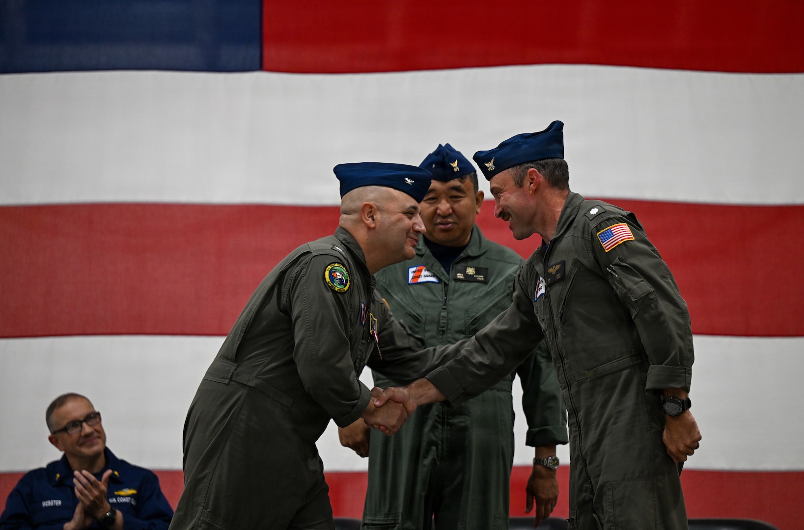 Capt. Neal Corbin (left) and Cmdr. Michael Flint (right) shake hands after a change-of-command ceremony that Rear Adm. Arex Avanni (center) presided over at Coast Guard Air Station Astoria in Warrenton, Ore., July 16, 2026. Corbin has served as Coast Guard Air Station Astoria’s commanding officer since 2024. (U.S. Coast Guard photo by Petty Officer 3rd Class William Kirk)