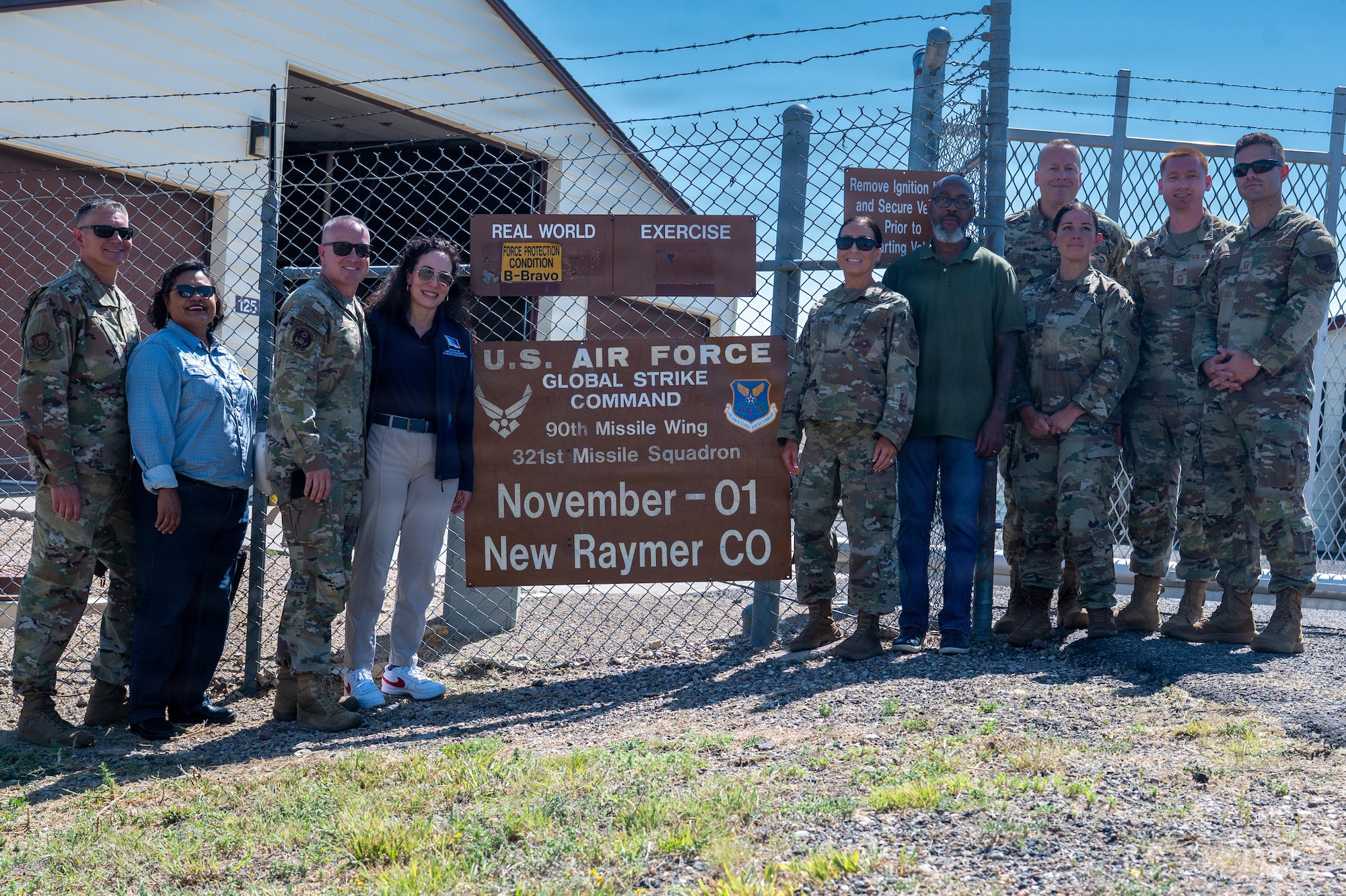 A photo of Chief Master Sergeant of the Air Force David R. Wolfe and the group accompanying him pose for a photo in front of the sign for November-01 a missile alert facility in Raymer, Colorado.