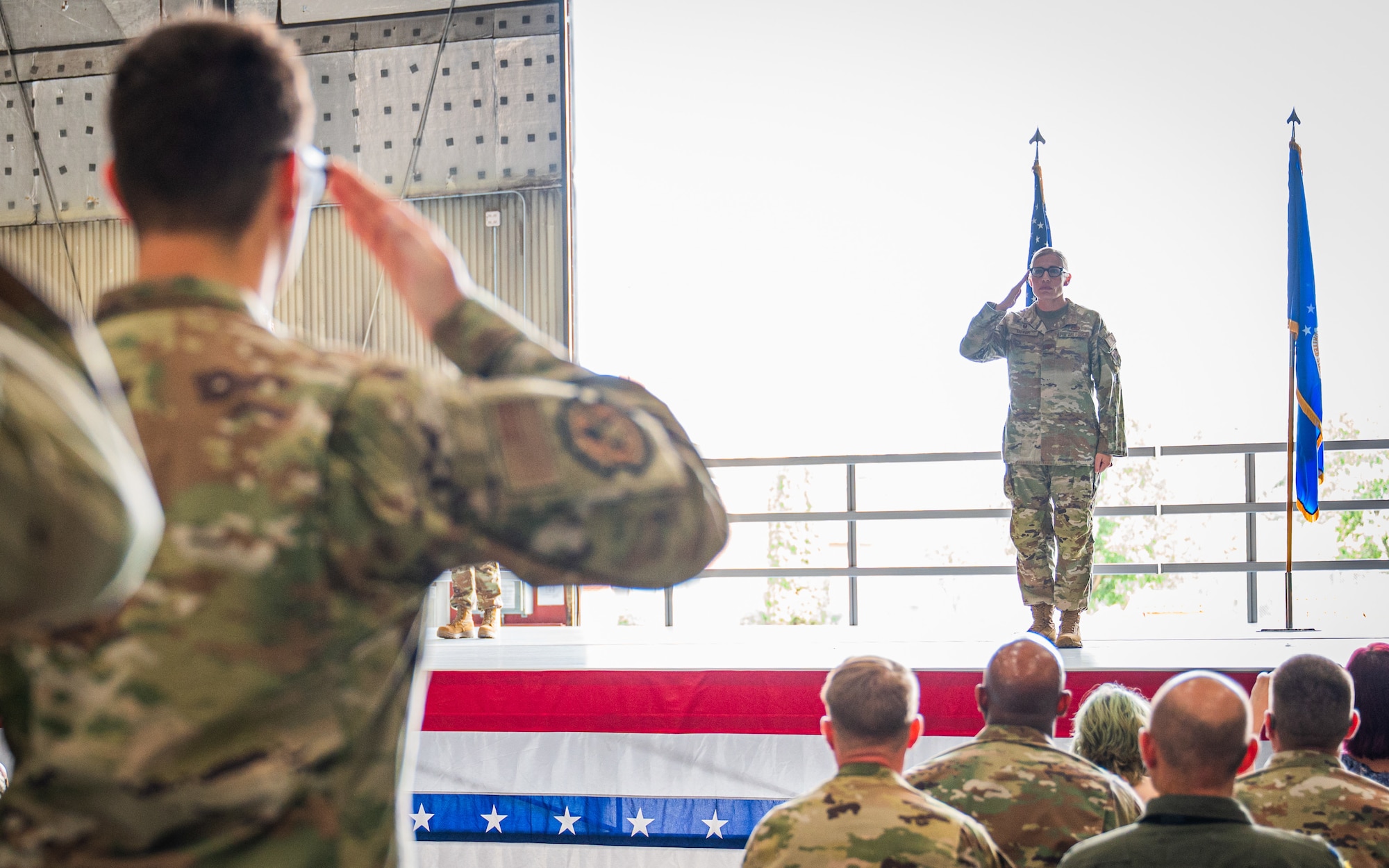 A photo of a woman standing on a stage giving a salute.