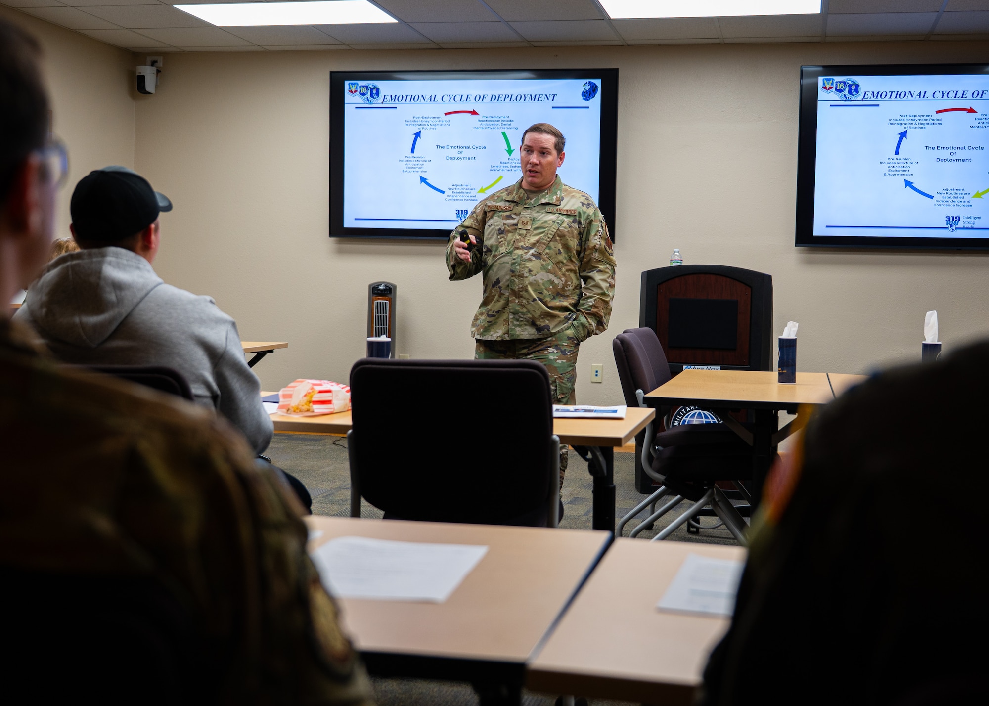 A photo of a man standing at the front of a room giving a briefing.