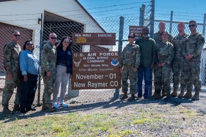 A photo of Chief Master Sergeant of the Air Force David R. Wolfe and the group accompanying him pose for a photo in front of the sign for November-01 a missile alert facility in Raymer, Colorado.