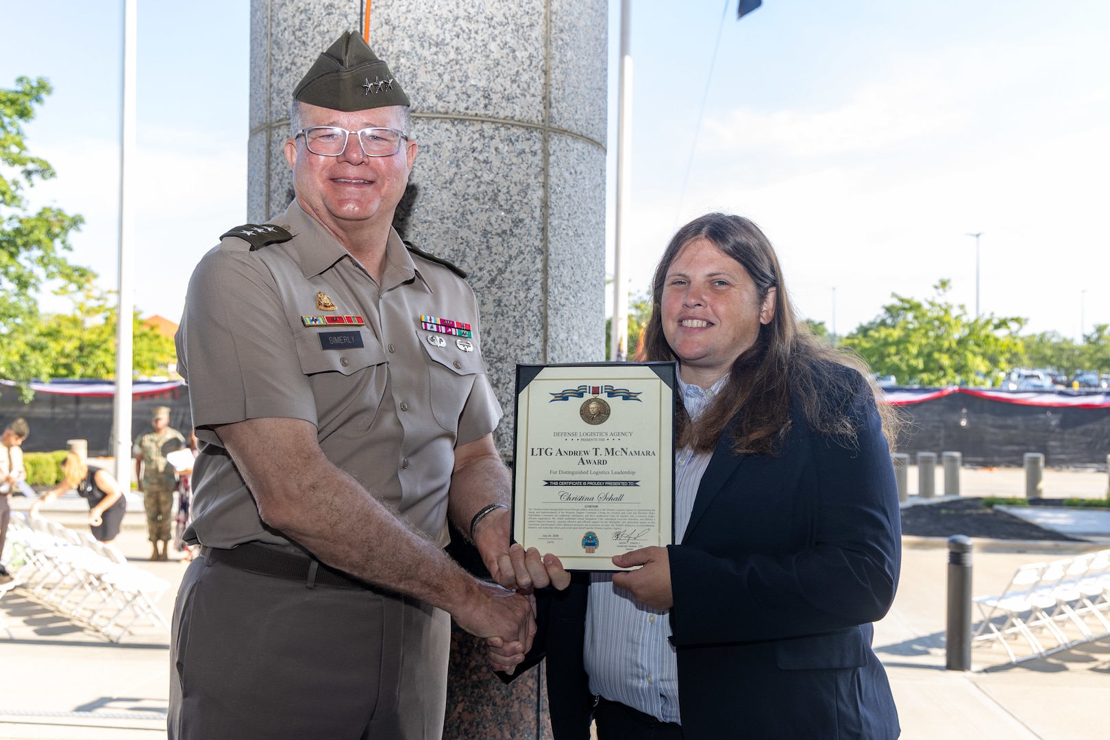 An Army general hands a award to a woman in a dark suit.
