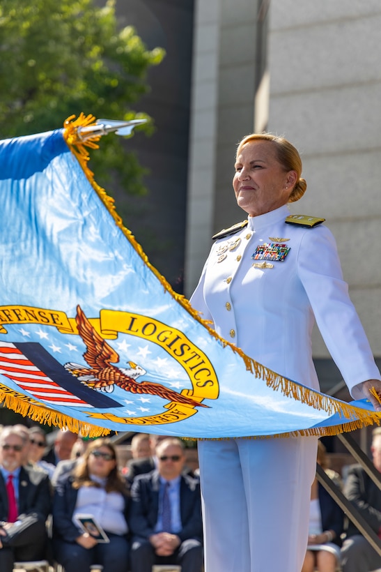 A woman in a Navy uniform holds a flag.