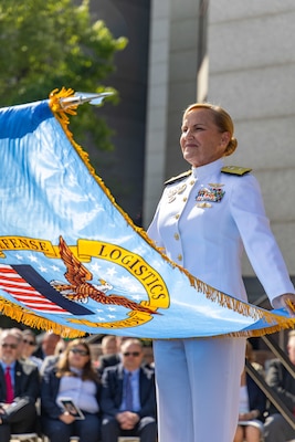 A woman in a Navy uniform holds a flag.