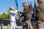 A man in a Army uniform hands a flag to a woman in a white Navy uniform.