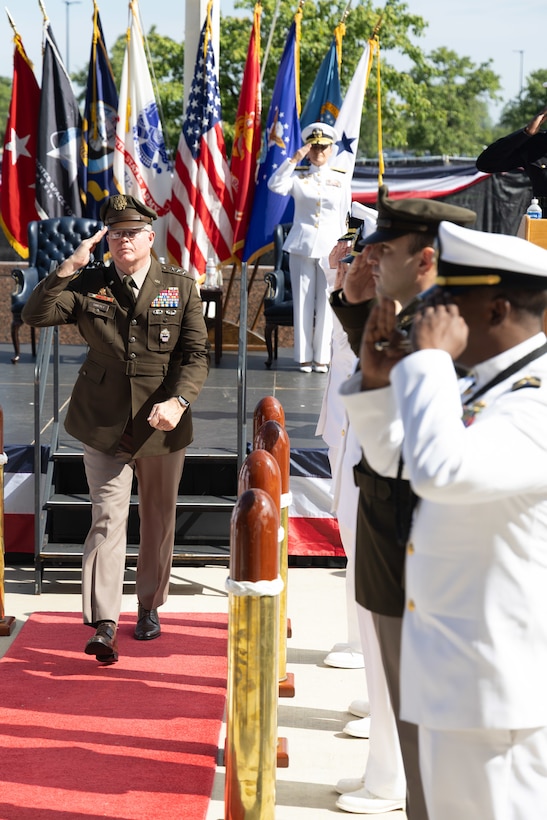 A man in a dress Armyuniform marches off stage in between people in uniform.