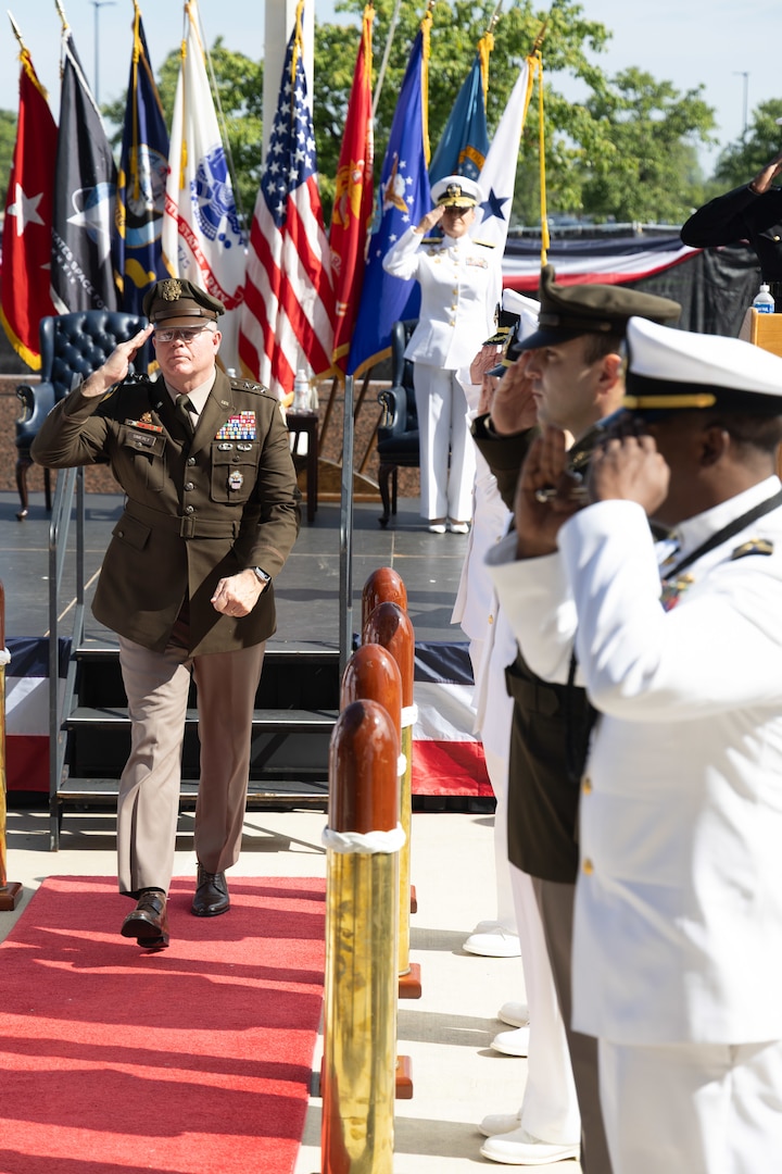 A man in a dress Armyuniform marches off stage in between people in uniform.